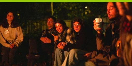 Jugendliche sitzen am Lagerfeuer zusammen und lachen.