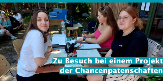 Drei Jugendliche sitzen draußen an einem Tisch und arbeiten kreativ mit Zettel und Stift.