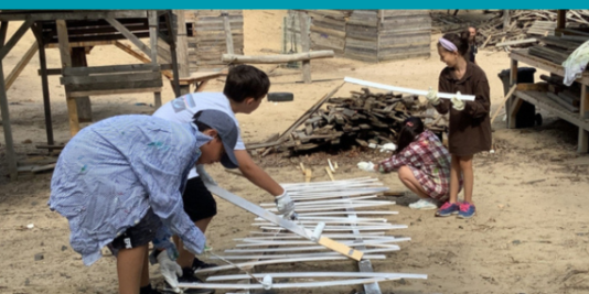 In einem Sandkasten bauen vier Kinder und Jugendliche an einem handwerklichen Projekt.