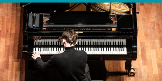 Ein Musiker in dunklem Pullover musiziert an einem Flügel. Fotografiert von oben.