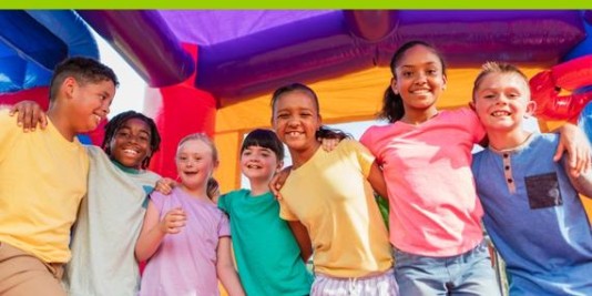 Kinder stehen in einer Hüpfburg nebeneinander in einer Reihe und haben die Arme auf die jeweils anderen Schultern gelegt.