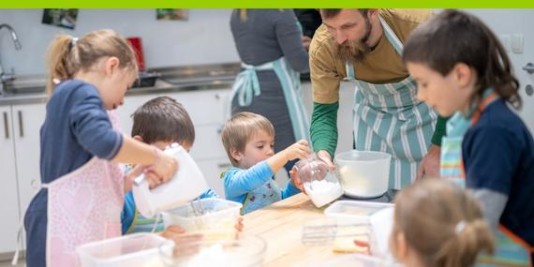Kinder stehen um einem Tisch herum und vermischen Backzutaten in verschiedenen Schüsseln.