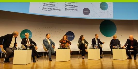 Menschen sitzen auf Stühlen auf einem Podium und unterhalten sich.