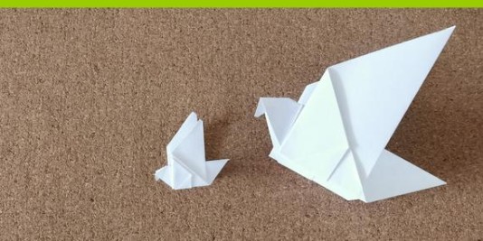 Zwei Origamitauben aus weißem Papier liegen auf braunem Untergrund.