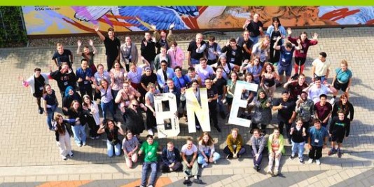 Eine Luftaufnahme einer Gruppe Jugendlicher, die die übergroßen Buchstaben B, N und E in die Luft halten.