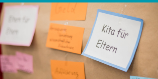Zettel an einer Pinnwand. Im Fokus ein Zettel mit dem folgenden Text: Kita für Eltern