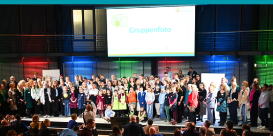 Gruppenfoto mit vielen Teilnehmenden der Förderpreisverleihung "Verein(t) für gute Kita und Schule" auf der Bühne des Stiftungsforums am Brandenburger Platz