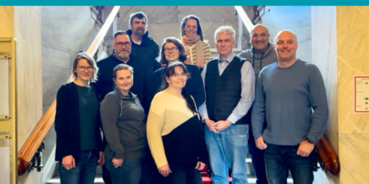 eine Gruppe Erwachsener steht in drei Reihen auf einer Treppe, alle schauen in die Kamera