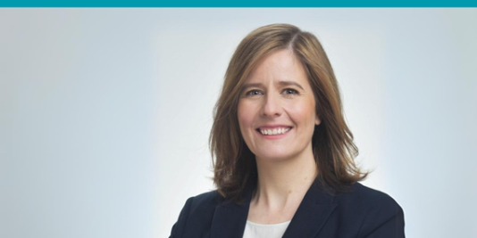 4 Menschen stehen nebeneinander, Arm in Arm und lächeln nach vorne in die Kamera