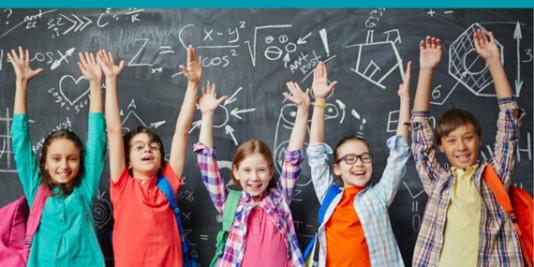 fünf Kinder stehen nebeneinander vor einer mit mathematischen Formeln vollgeschriebenen Schultafel und haben die Arme nach oben gestreckt