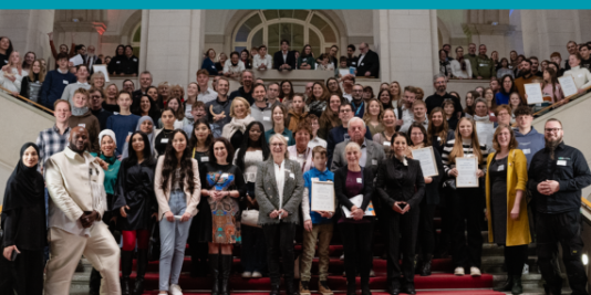 Zwei Mädchen mit Schutzbrillen und Werkzeugen in der Hand schauen glücklich und stolz in die Kamera.
