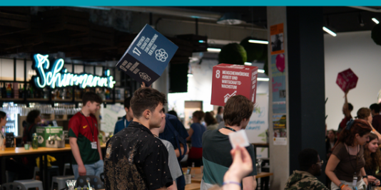 Teilnehmer*innen der youcoN 2023 halten große SDG-Würfel in die Luft 