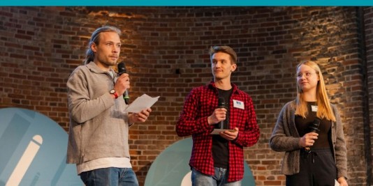 drei junge Menschen stehen auf einer Bühne mit Mikrofonen in der Hand